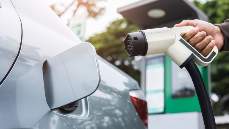 Electric car plugged into fast charger as driver connects charging cable